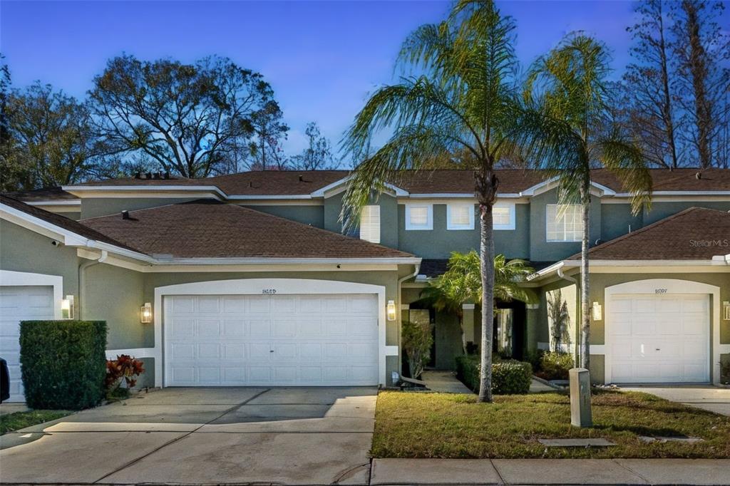 A two-story townhouse exterior with two white garage doors, green siding, and a palm tree — 8809 CASABLANCA WAY, TAMPA, FL
