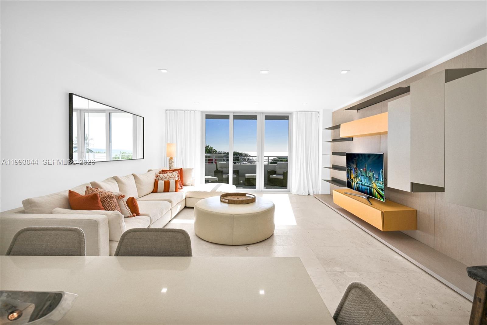 A modern living room features a large sectional sofa, a round ottoman, and wall-mounted cabinetry — 5555 Collins Ave # 3N, Miami Beach FL 33140, MIAMI BEACH, FL