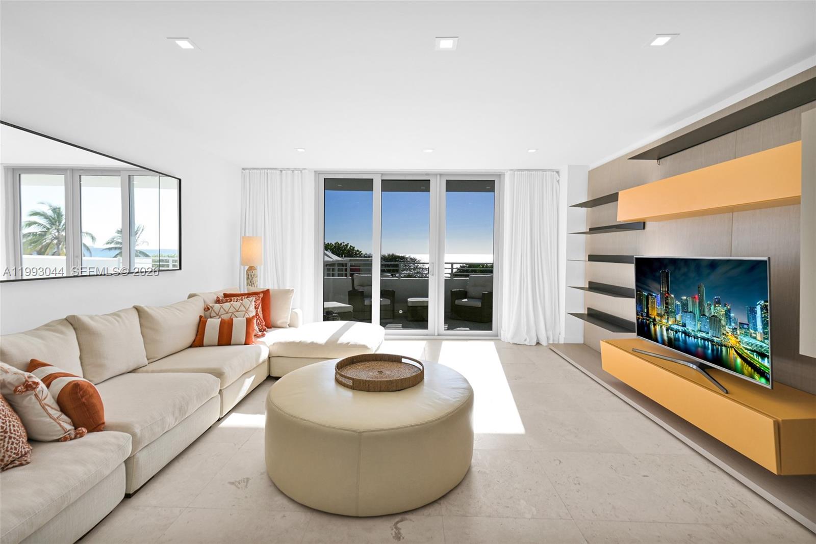 A modern living room features a large sectional sofa, circular ottoman, and built-in media shelving — 5555 Collins Ave # 3N, Miami Beach FL 33140, MIAMI BEACH, FL