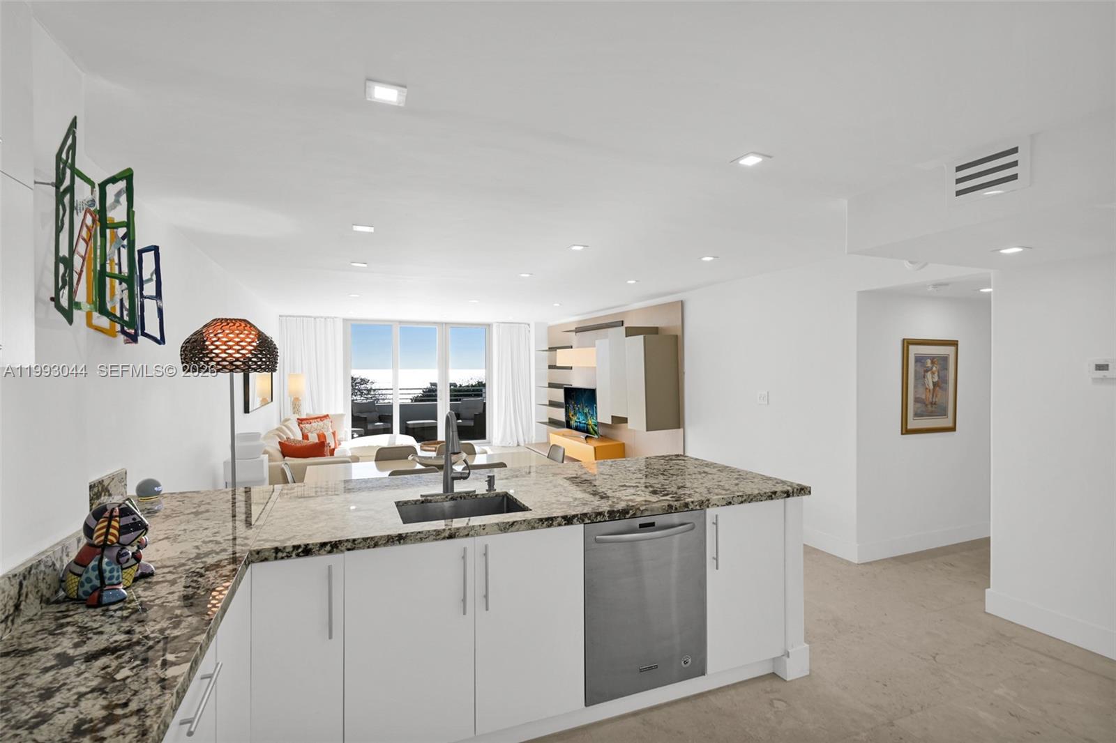 A kitchen with granite countertops and white cabinets overlooks a living area with balcony access — 5555 Collins Ave # 3N, Miami Beach FL 33140, MIAMI BEACH, FL