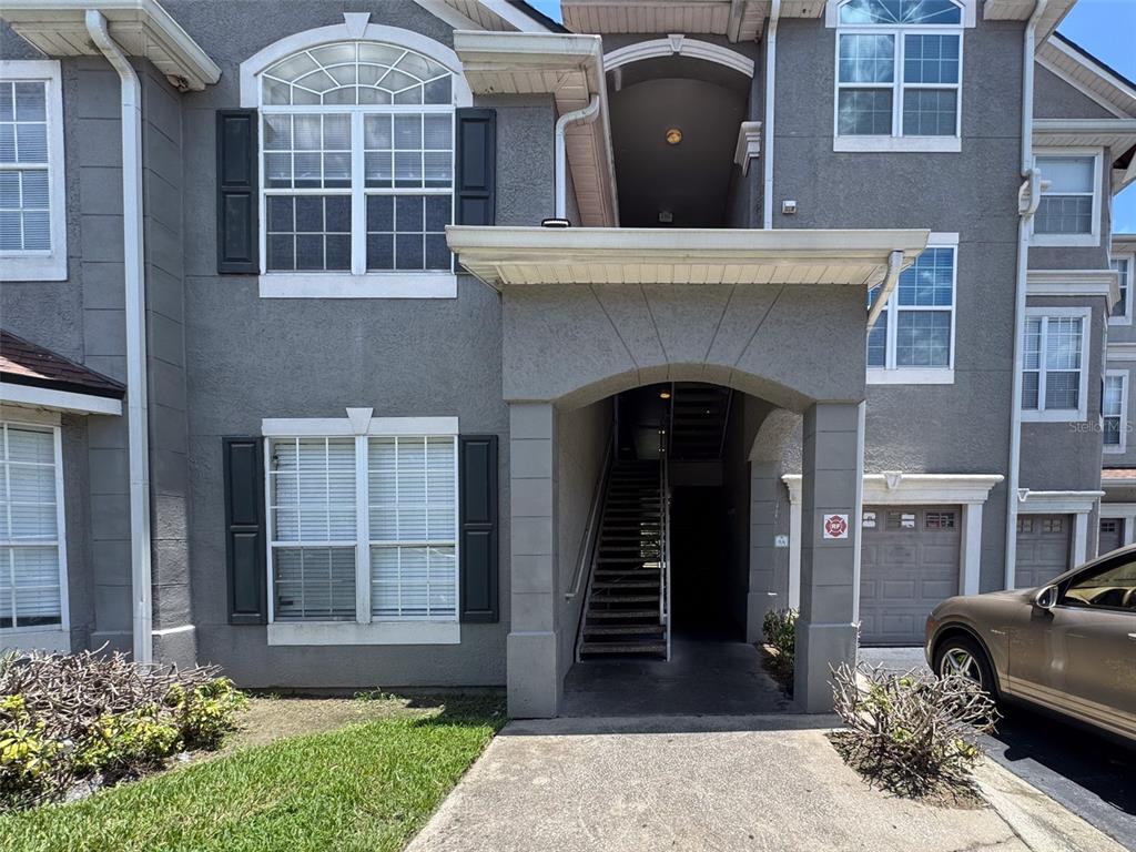 A gray stucco multi-story building features a covered entryway with stairs and an attached garage — 3373 S KIRKMAN ROAD UNIT 936, ORLANDO, FL
