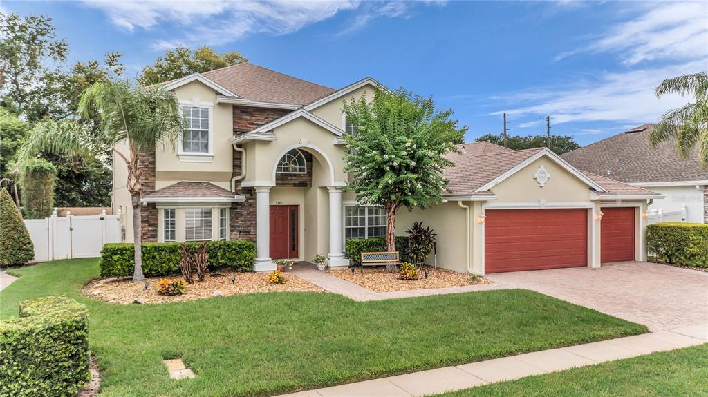 A two-story suburban house with a tan stucco exterior, stone accents, and a three-car garage — 3342 HERRINGRIDGE DRIVE, ORLANDO, FL