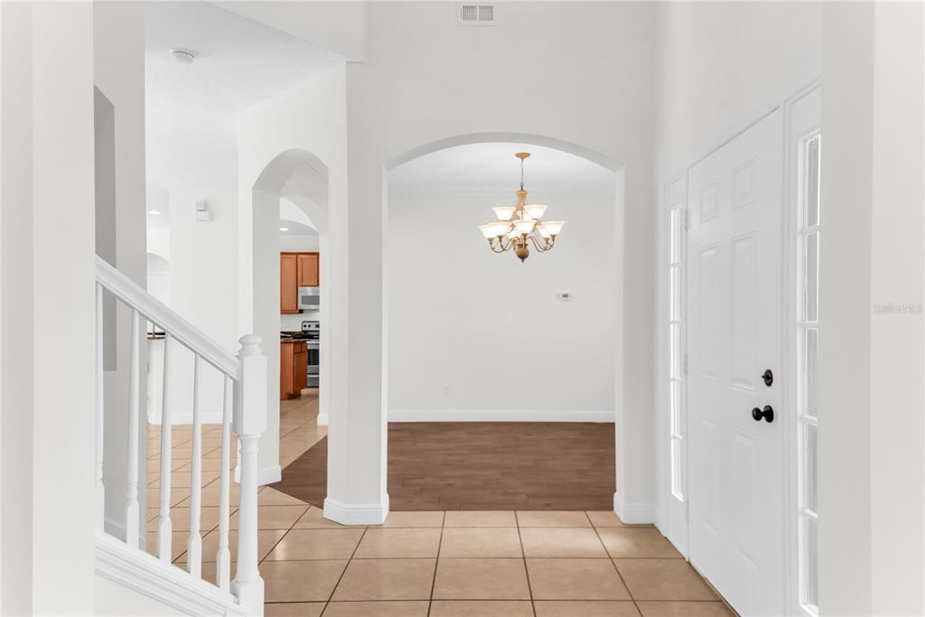An entryway with tile flooring, a white staircase, and an arched opening to a dining area — 3342 HERRINGRIDGE DRIVE, ORLANDO, FL