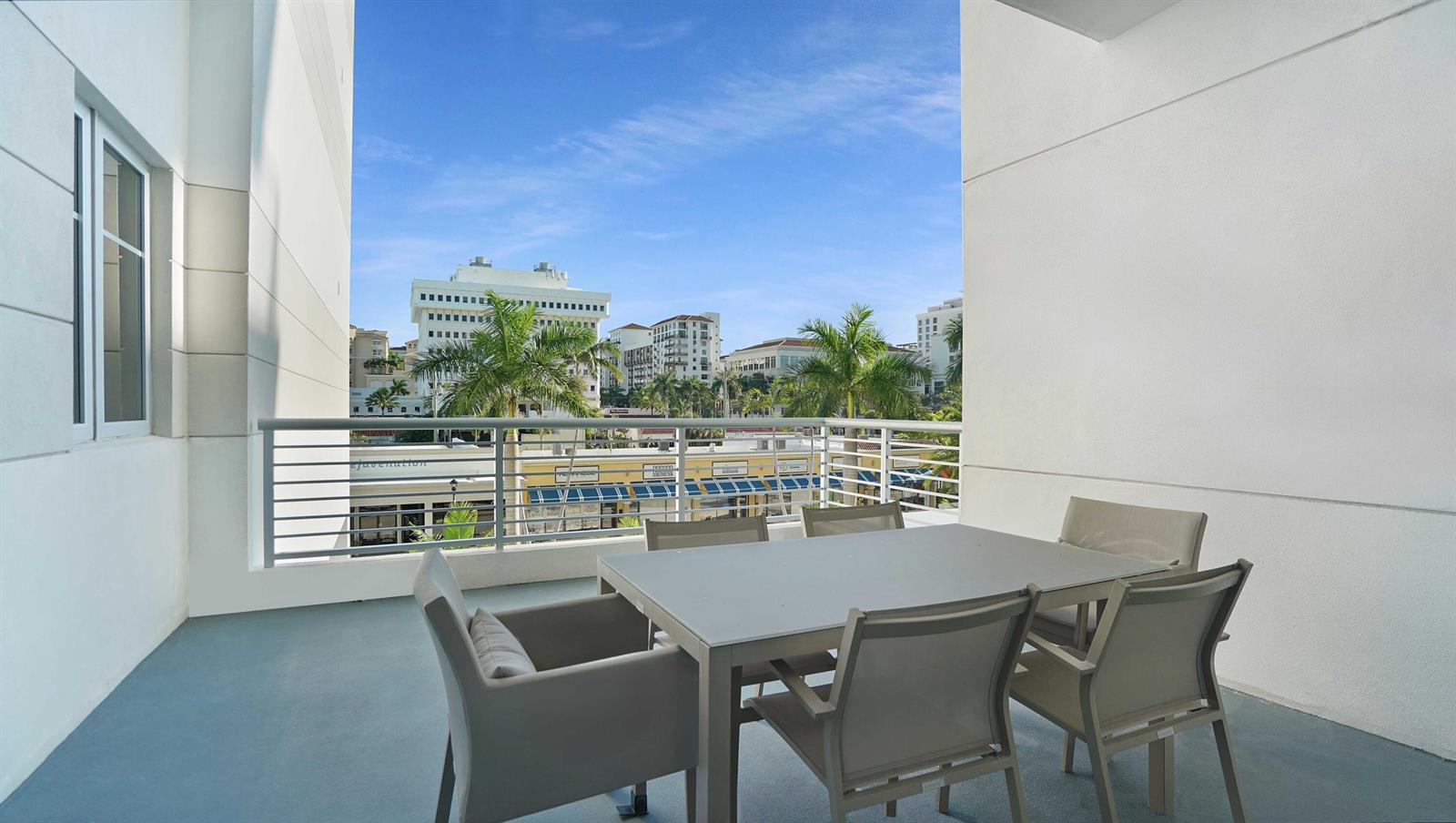 A balcony with a dining set overlooks a city street with palm trees and buildings — 155 E Boca Raton Road # 301, Boca Raton FL 33432, BOCA RATON, FL