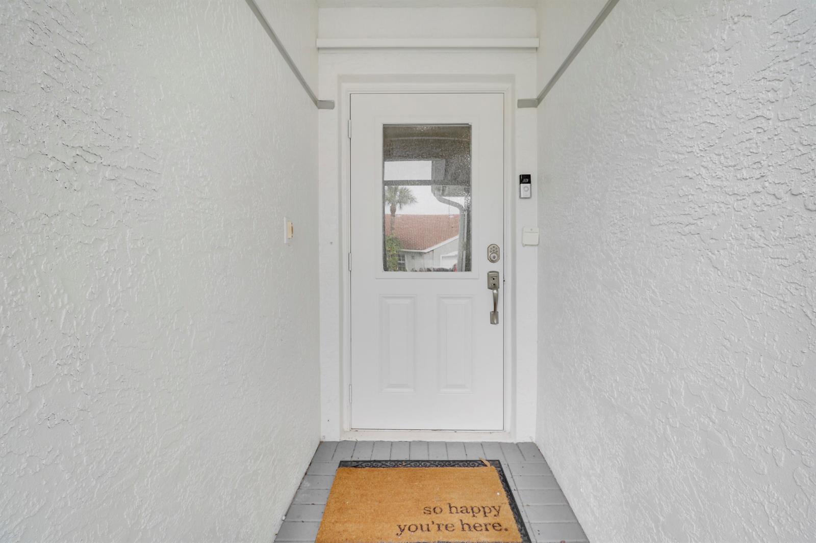 A white front door with a glass pane sits at the end of a covered entryway — 8063 Dolomtian Way, Boynton Beach FL 33472, BOYNTON BEACH, FL