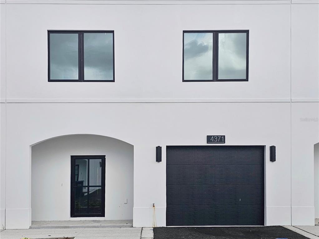 A modern two-story townhouse exterior features a white facade, black-framed windows, a front door, and a garage — 4371 CAMBIO GARDENS COURT, TAMPA, FL
