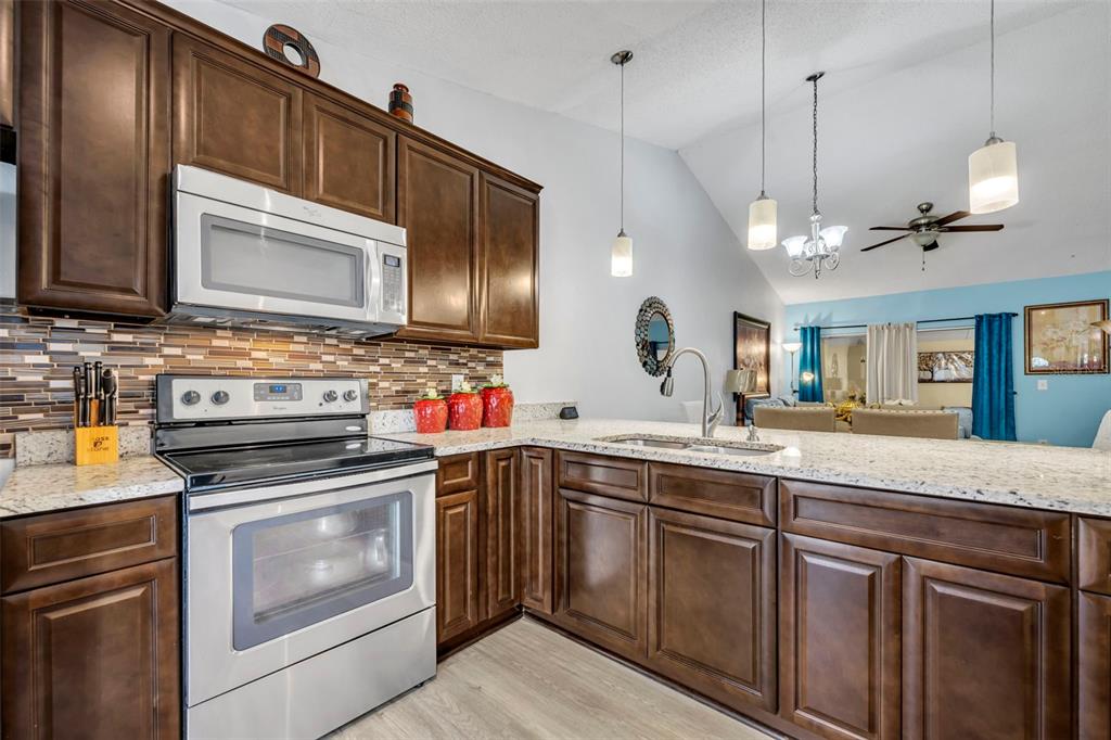 A kitchen features dark wood cabinets, granite countertops, stainless steel appliances, and a tiled backsplash — 3204 TIDEWATER DRIVE, KISSIMMEE, FL