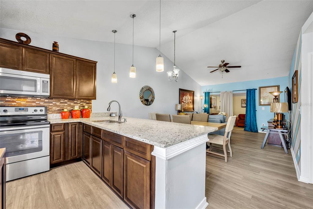 A kitchen with dark wood cabinets and granite countertops opens into a living and dining area — 3204 TIDEWATER DRIVE, KISSIMMEE, FL
