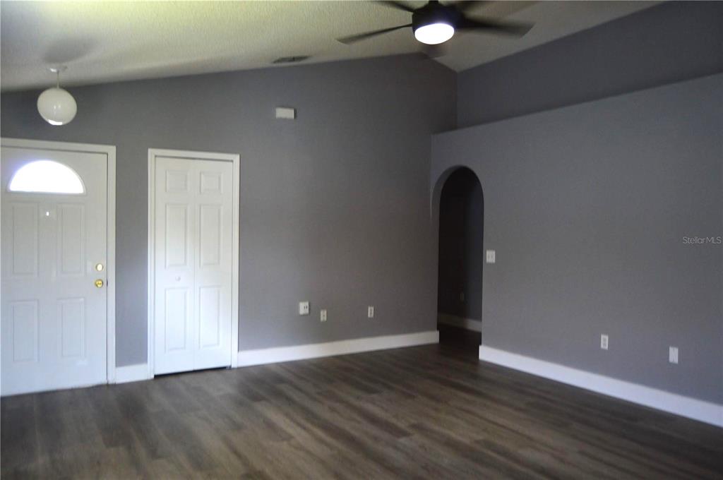 A living room with gray walls, wood-look flooring, a vaulted ceiling, and an arched doorway — 424 DELICATA DRIVE, ORLANDO, FL