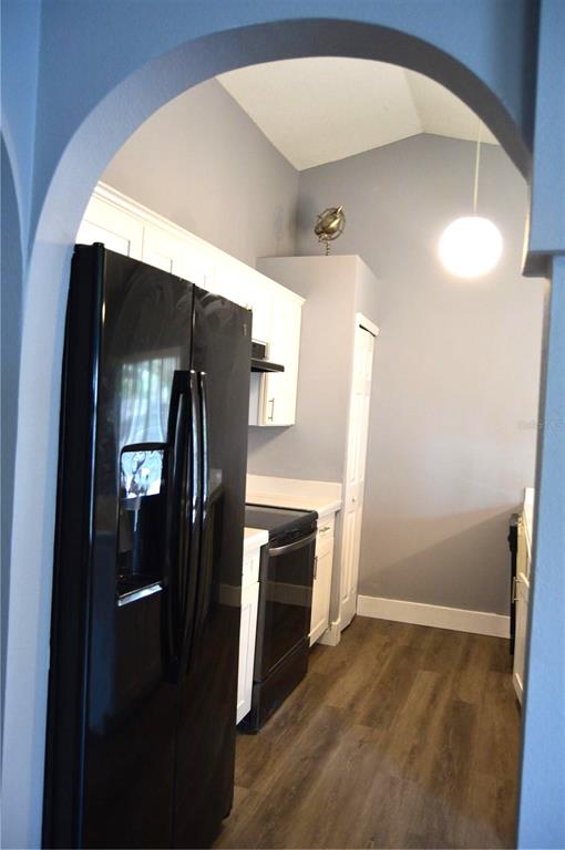 A kitchen with white cabinets, black appliances, and wood-look flooring viewed through an arched doorway — 424 DELICATA DRIVE, ORLANDO, FL