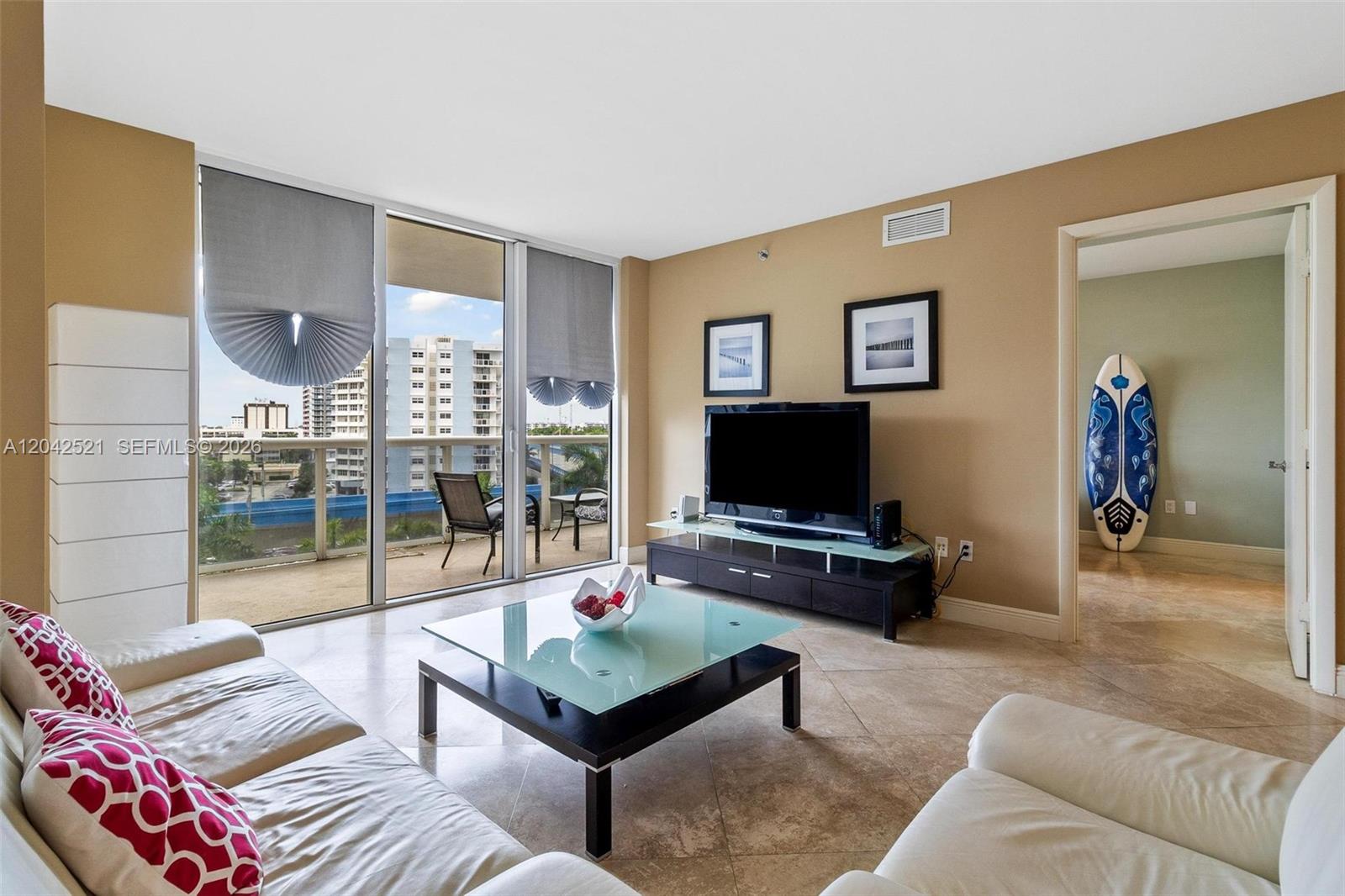 A living room features a glass coffee table, white leather sofas, and a balcony view — 1800 S Ocean Dr # 608, Hallandale Beach FL 33009, HALLANDALE BEACH, FL