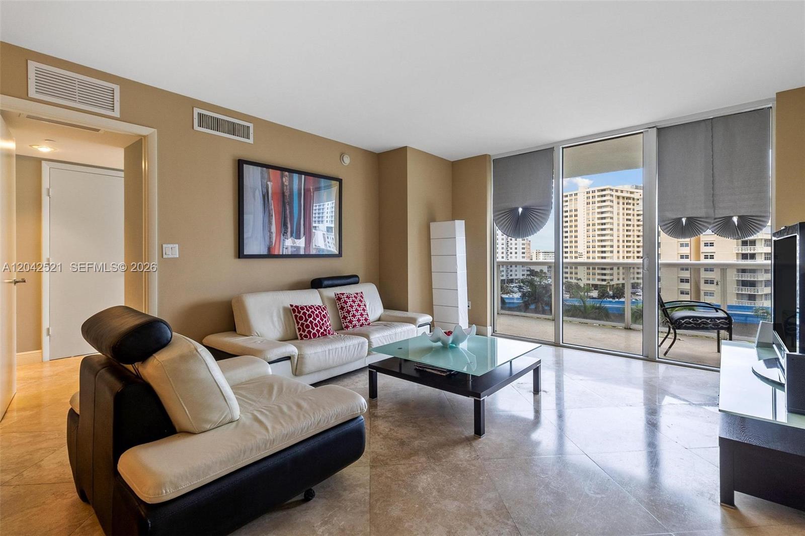 A living room features beige walls, tile flooring, a glass coffee table, and balcony access — 1800 S Ocean Dr # 608, Hallandale Beach FL 33009, HALLANDALE BEACH, FL