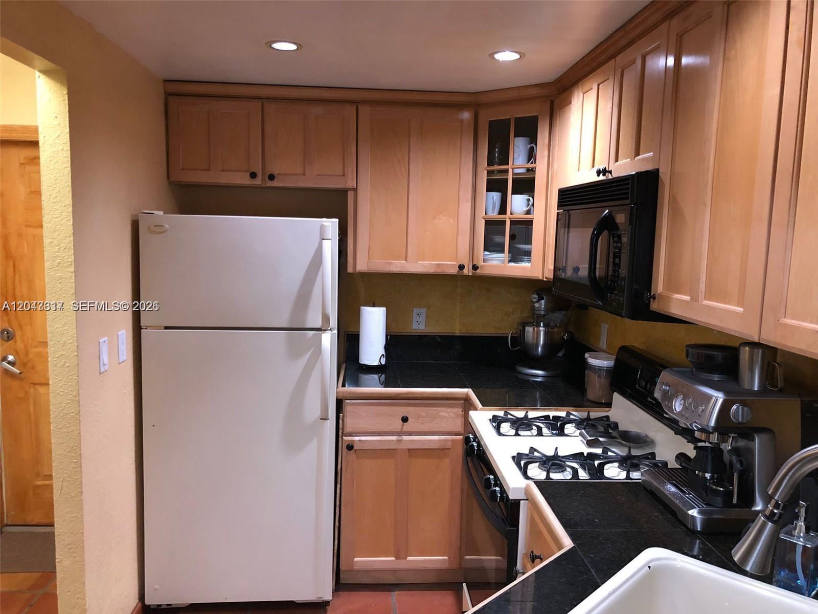 A kitchen features light wood cabinets, black countertops, a white refrigerator, and a gas stove — 6705 N Kendall Dr # 312, Pinecrest FL 33156, PINECREST, FL