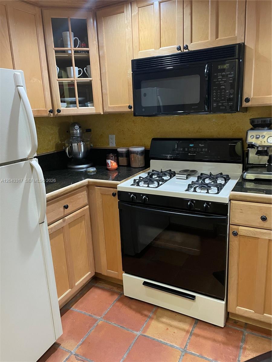 A kitchen features light wood cabinets, black countertops, a white stove, and terracotta floor tiles — 6705 N Kendall Dr # 312, Pinecrest FL 33156, PINECREST, FL