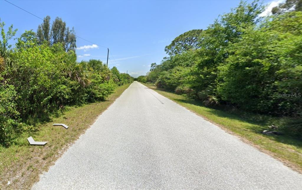 A paved road stretches into the distance, flanked by dense green trees and vegetation — 9366 LOYOLA AVENUE, ENGLEWOOD, FL