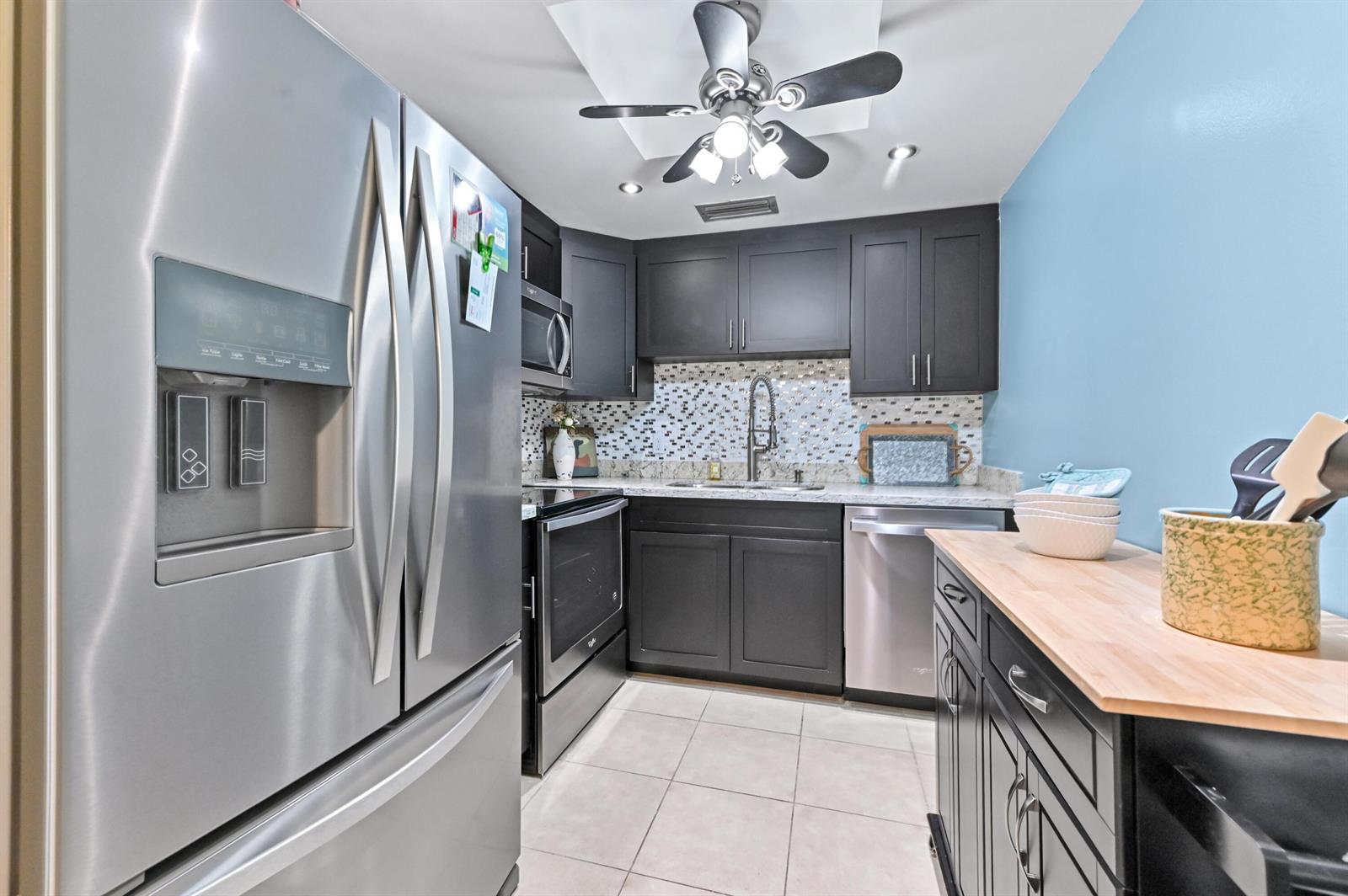 A kitchen features dark cabinetry, stainless steel appliances, a mosaic backsplash, and a ceiling fan — 196 Grantham F # 196, Deerfield Beach FL 33442, DEERFIELD BEACH, FL