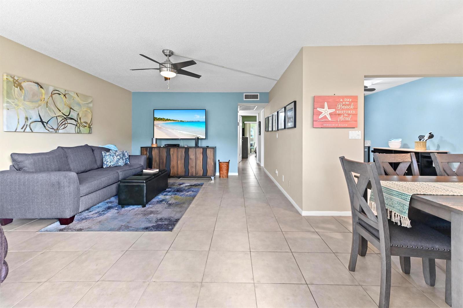 A living room with a grey sofa, blue accent wall, and tile flooring — 196 Grantham F # 196, Deerfield Beach FL 33442, DEERFIELD BEACH, FL