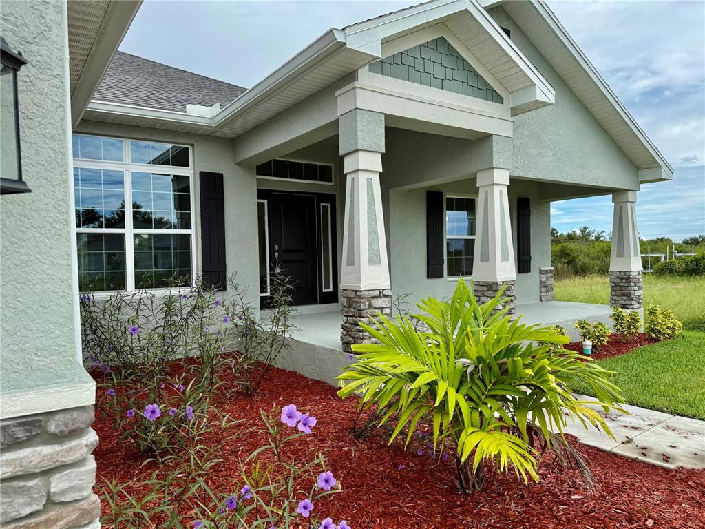 The exterior of a house features a covered porch with stone-based columns and landscaping — 13236 PACE CIRCLE, PORT CHARLOTTE, FL
