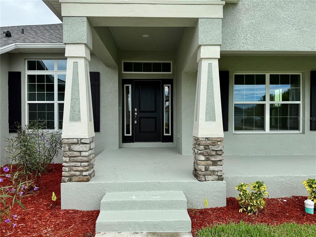 The front entrance features a covered porch with stone-based pillars and a dark front door — 13236 PACE CIRCLE, PORT CHARLOTTE, FL