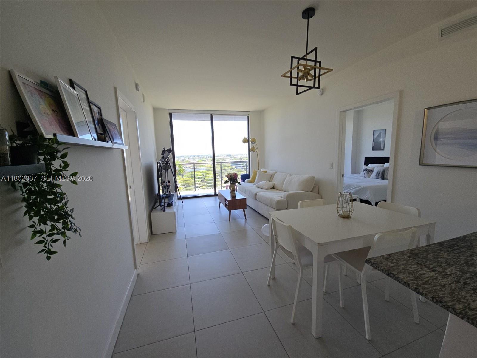 An open-concept living and dining area features white tile floors, a balcony, and a bedroom — 5350 NW 84th Ave # 1207, Doral FL 33166, DORAL, FL
