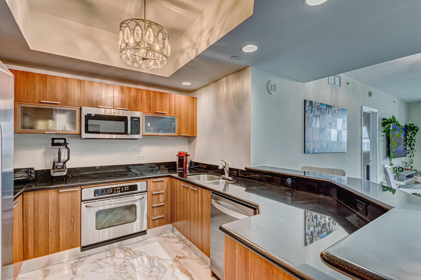 A modern kitchen features wood cabinets, black granite countertops, stainless steel appliances, and marble flooring — 2640 Lake Shore Drive # 2014, Riviera Beach FL 33404, RIVIERA BEACH, FL
