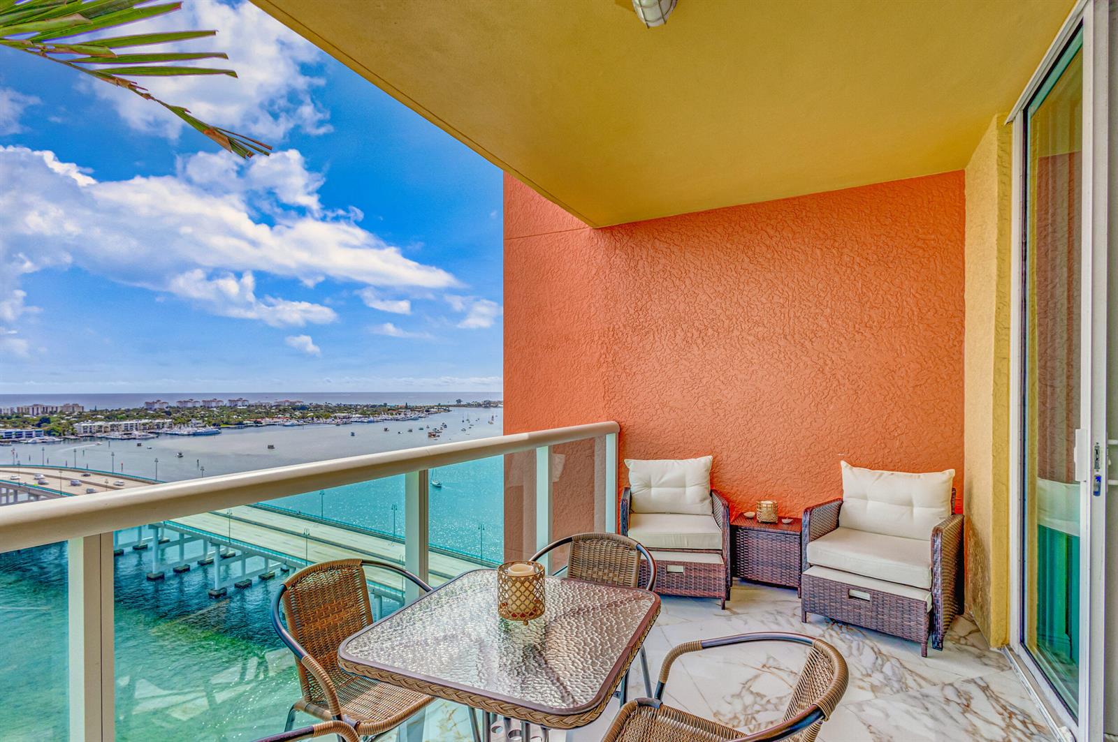 A balcony with wicker furniture overlooks a bridge, a bay, and a distant city skyline — 2640 Lake Shore Drive # 2014, Riviera Beach FL 33404, RIVIERA BEACH, FL