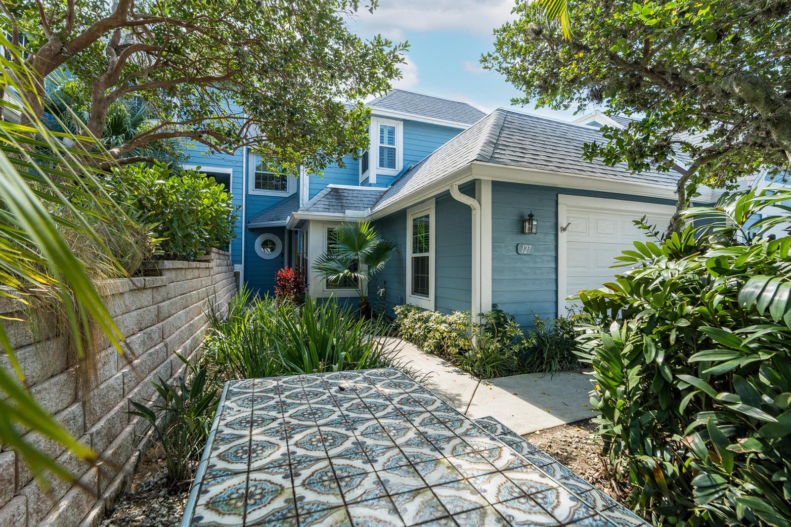 A blue two-story house with a white garage door and a tiled outdoor table — 127 Ocean Dunes Circle, Jupiter FL 33477, JUPITER, FL