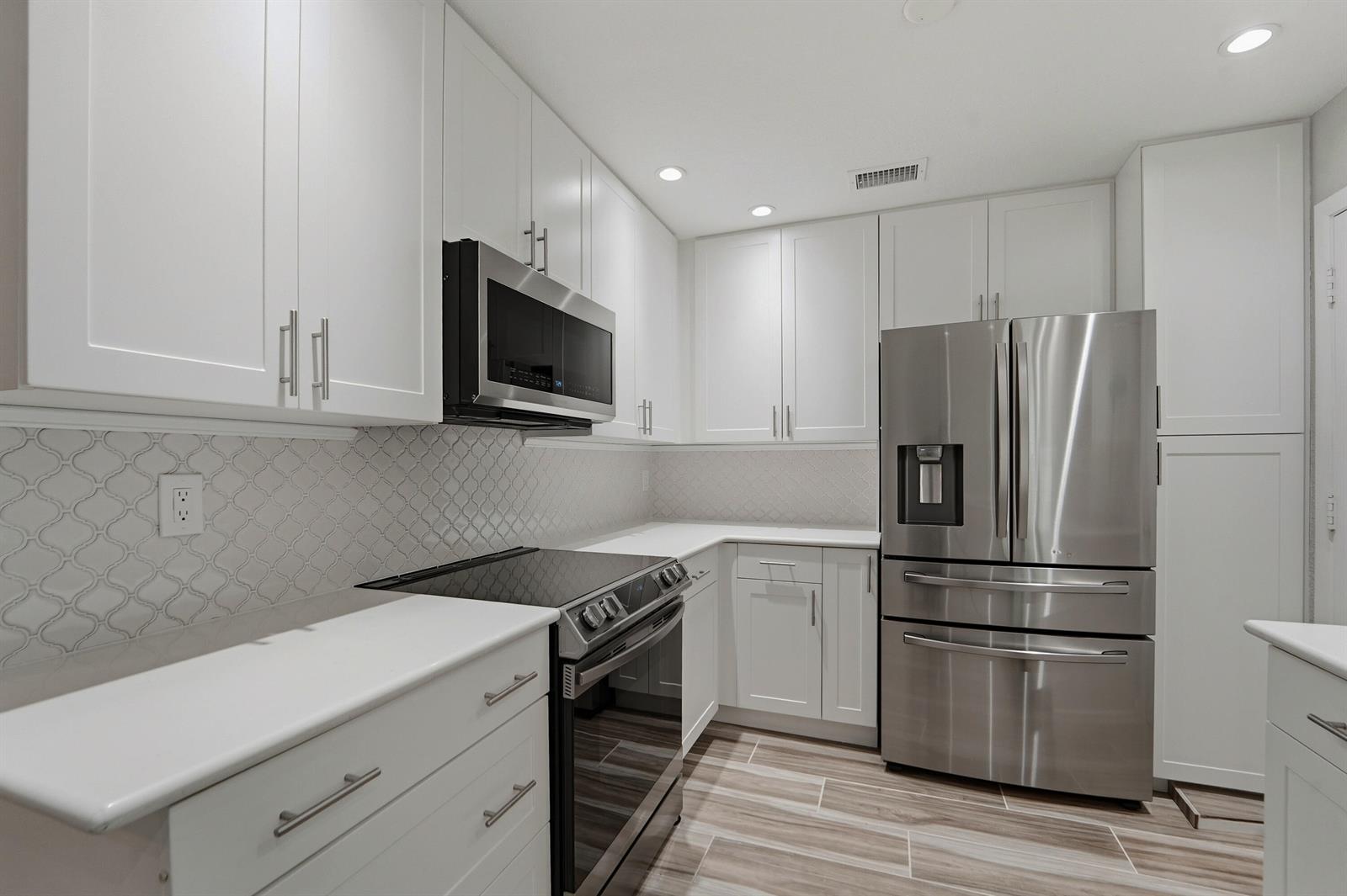 A kitchen with white cabinets, stainless steel appliances, and a patterned tile backsplash — 127 Ocean Dunes Circle, Jupiter FL 33477, JUPITER, FL