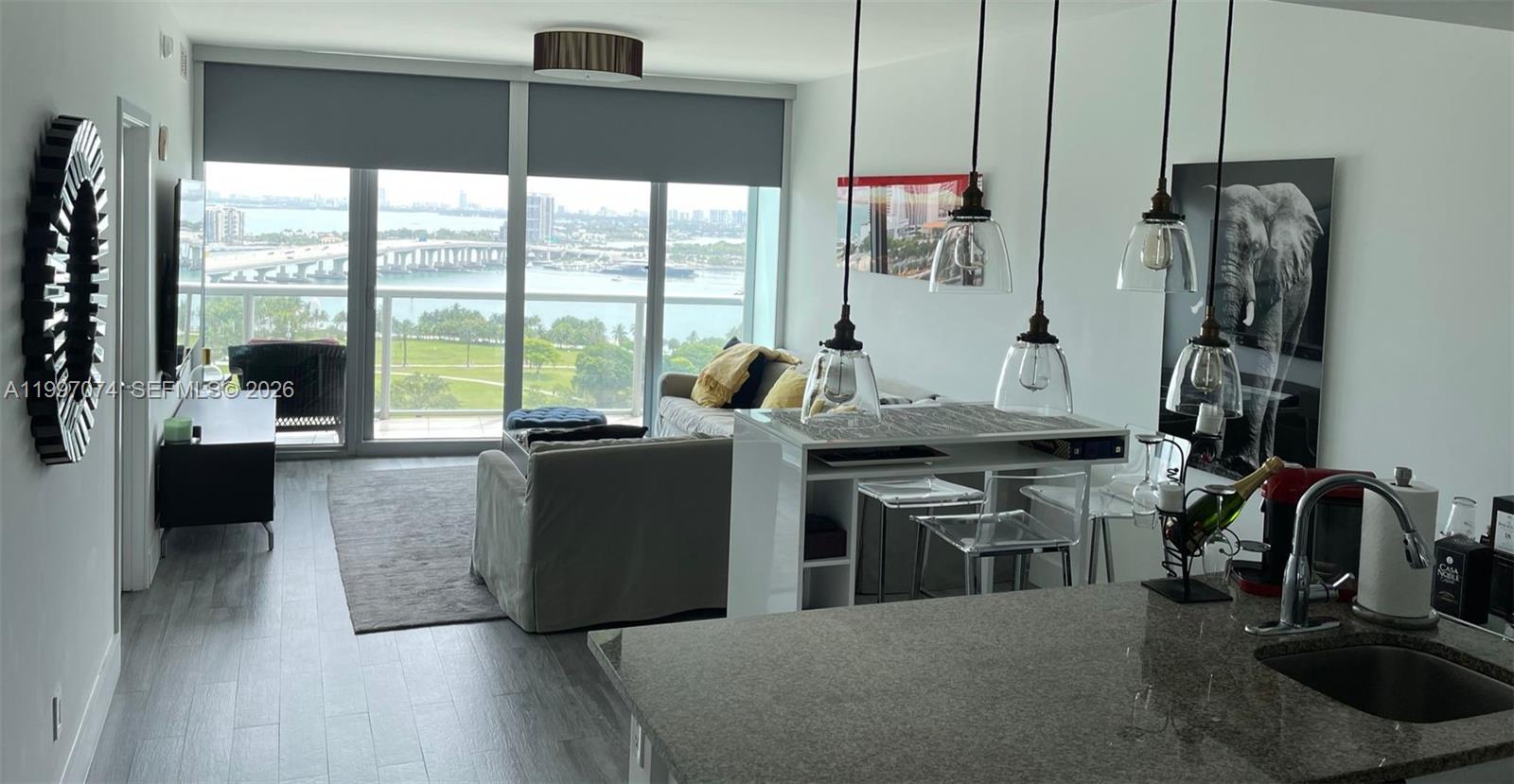 A modern apartment living area features a kitchen island, pendant lighting, and a balcony view — 888 Biscayne Blvd # 1810, Miami FL 33132, MIAMI, FL