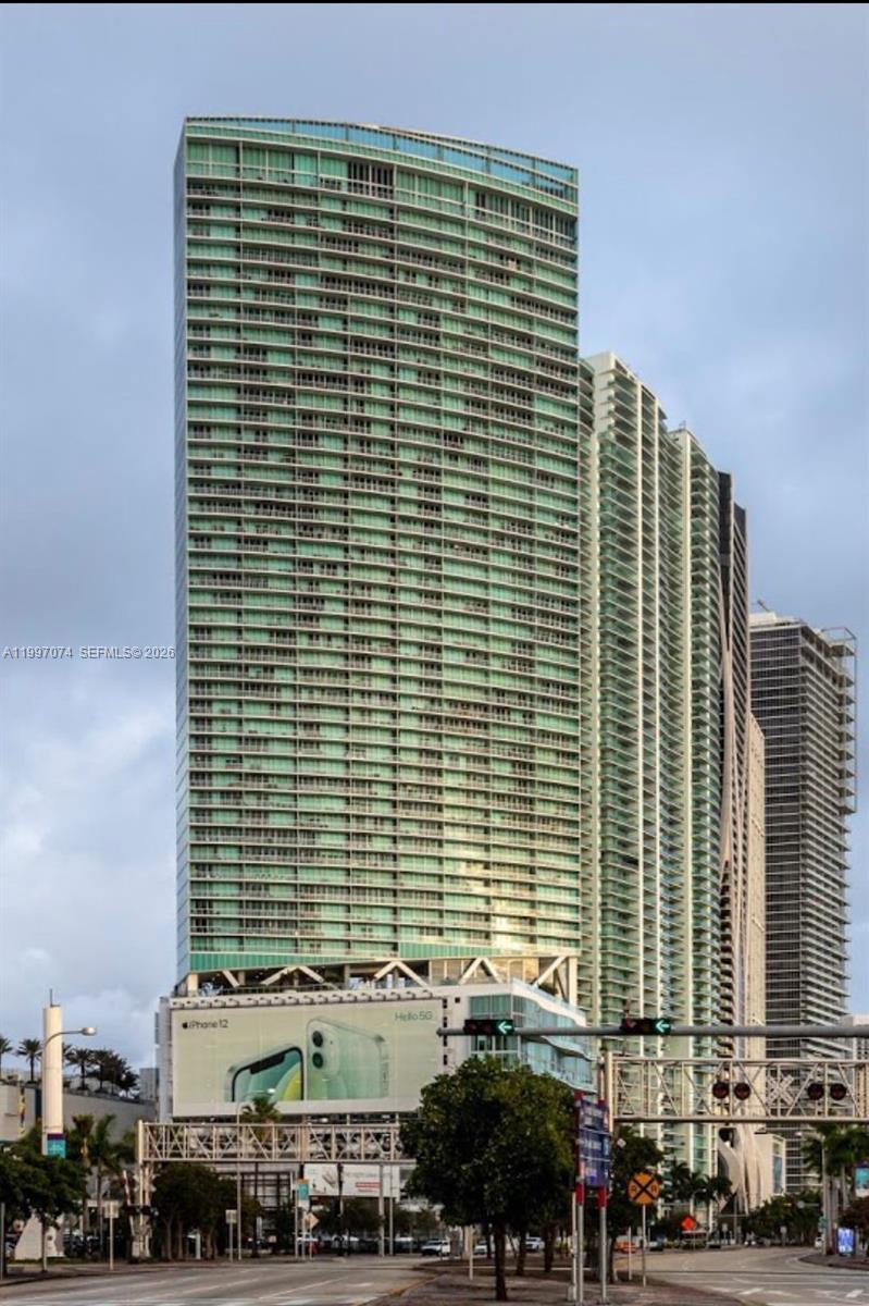 A tall, modern glass-facade residential skyscraper stands above a street with a large billboard — 888 Biscayne Blvd # 1810, Miami FL 33132, MIAMI, FL