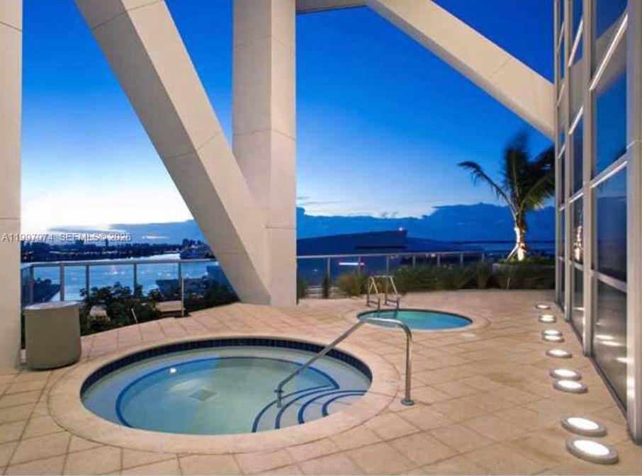 Two circular hot tubs sit on a tiled outdoor terrace overlooking a waterfront city view — 888 Biscayne Blvd # 1810, Miami FL 33132, MIAMI, FL
