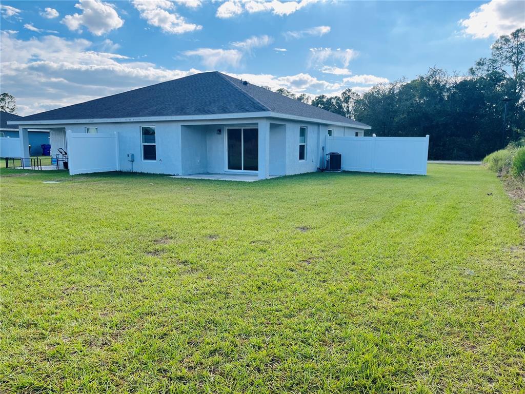 The rear exterior of a single-story house features a concrete patio and white vinyl fencing — 6801 DICKINSON DRIVE, SEBRING, FL