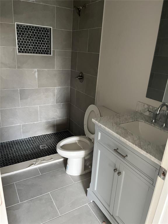 A bathroom features a gray vanity, a toilet, and a walk-in shower with tiled walls — 6801 DICKINSON DRIVE, SEBRING, FL
