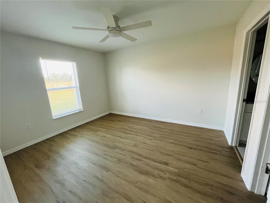 An empty bedroom features light-colored walls, wood-look flooring, a ceiling fan, and a window — 6801 DICKINSON DRIVE, SEBRING, FL