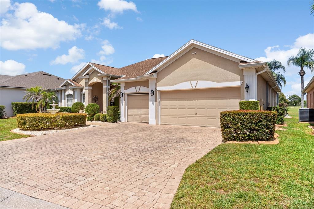 A beige single-story house with a paver driveway, two-car garage, and a front yard fountain — 622 GOLF COURSE PARKWAY, DAVENPORT, FL