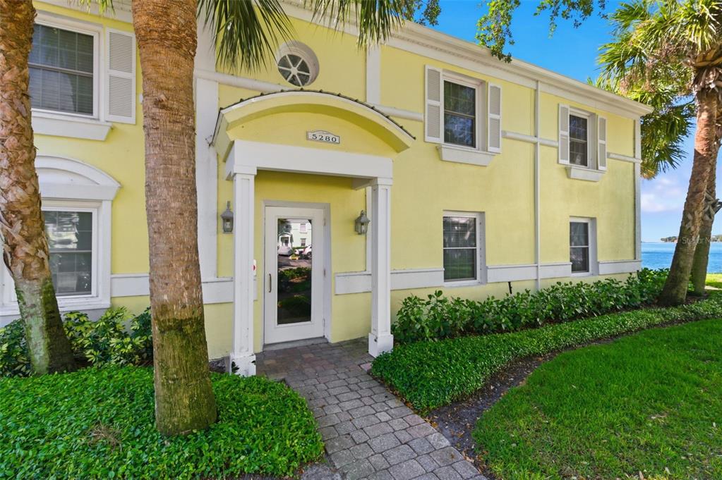 A yellow two-story building features a covered entryway with a stone walkway and palm trees — 5280 COQUINA KEY DRIVE SE UNIT A furnished seasonal, ST PETERSBURG, FL