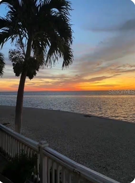 A palm tree stands near a wooden railing overlooking a beach at sunset — 5280 COQUINA KEY DRIVE SE UNIT A furnished seasonal, ST PETERSBURG, FL
