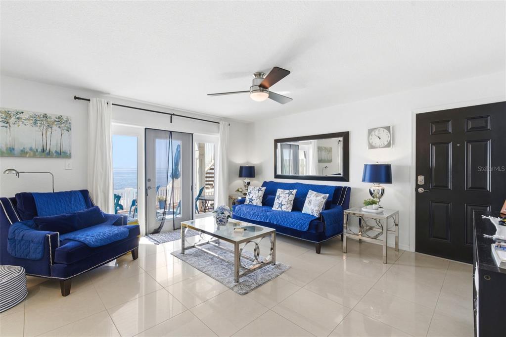 A living room features blue furniture, a glass coffee table, and a sliding door to a balcony — 5280 COQUINA KEY DRIVE SE UNIT A furnished seasonal, ST PETERSBURG, FL