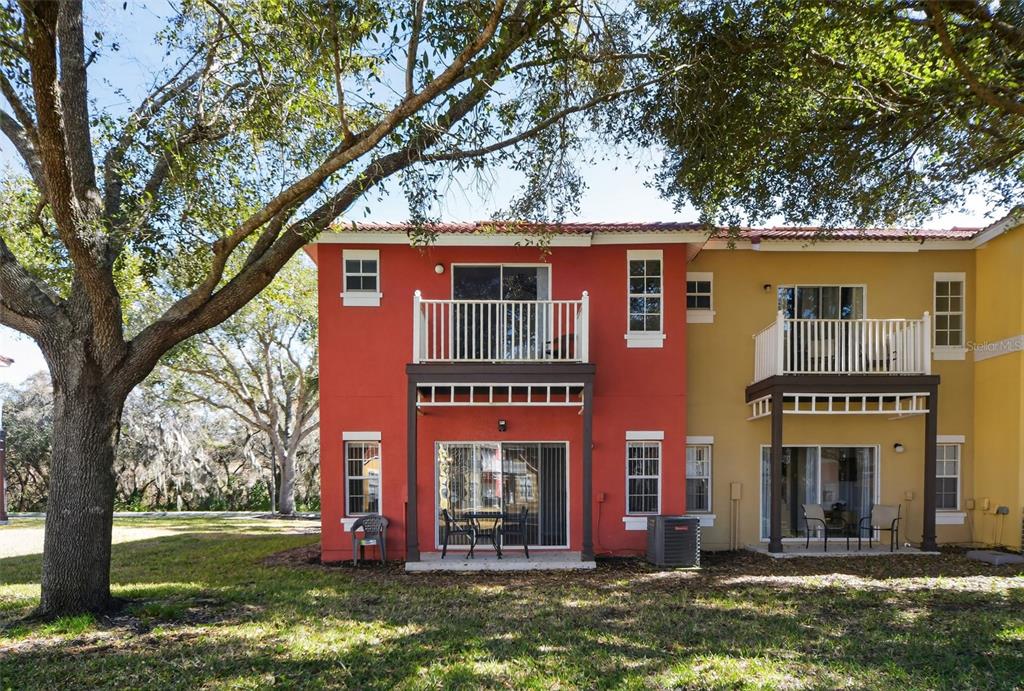 The exterior of a two-story red and yellow townhouse with balconies and sliding glass doors — 8538 CRYSTAL COVE LOOP, KISSIMMEE, FL