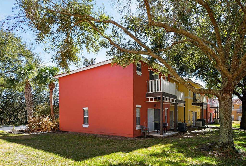 A bright red two-story townhouse exterior with a small balcony and a grassy yard — 8538 CRYSTAL COVE LOOP, KISSIMMEE, FL