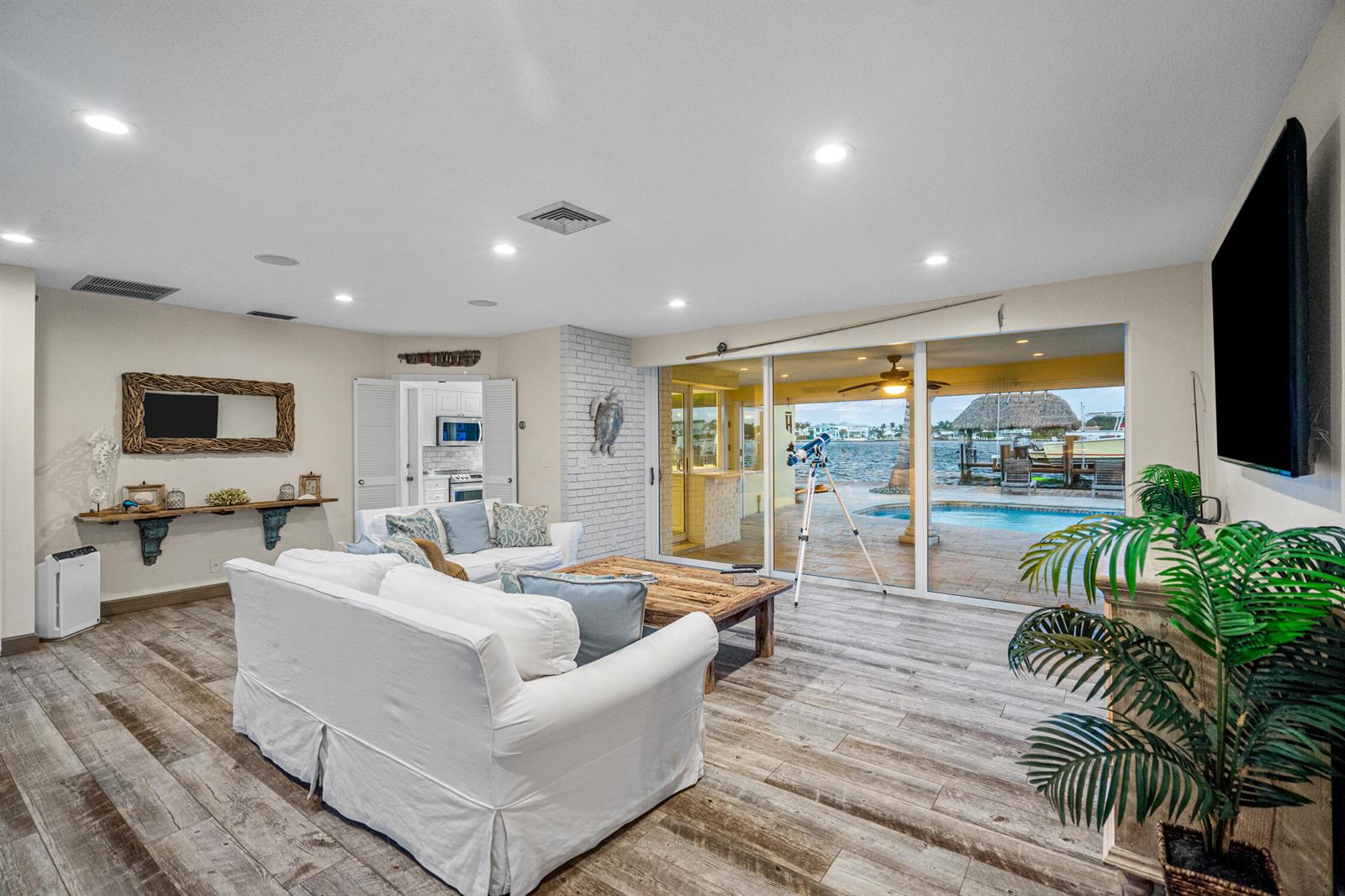 A living room with white sofas, wood-look tile floors, and sliding doors overlooking a pool — 844 East Drive, Boynton Beach FL 33435, BOYNTON BEACH, FL