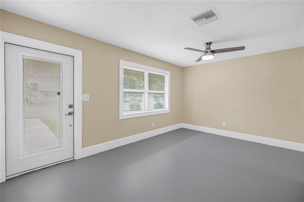 An empty room features gray flooring, beige walls, a ceiling fan, and a glass-paneled door — 1416 38TH AVENUE N, ST PETERSBURG, FL