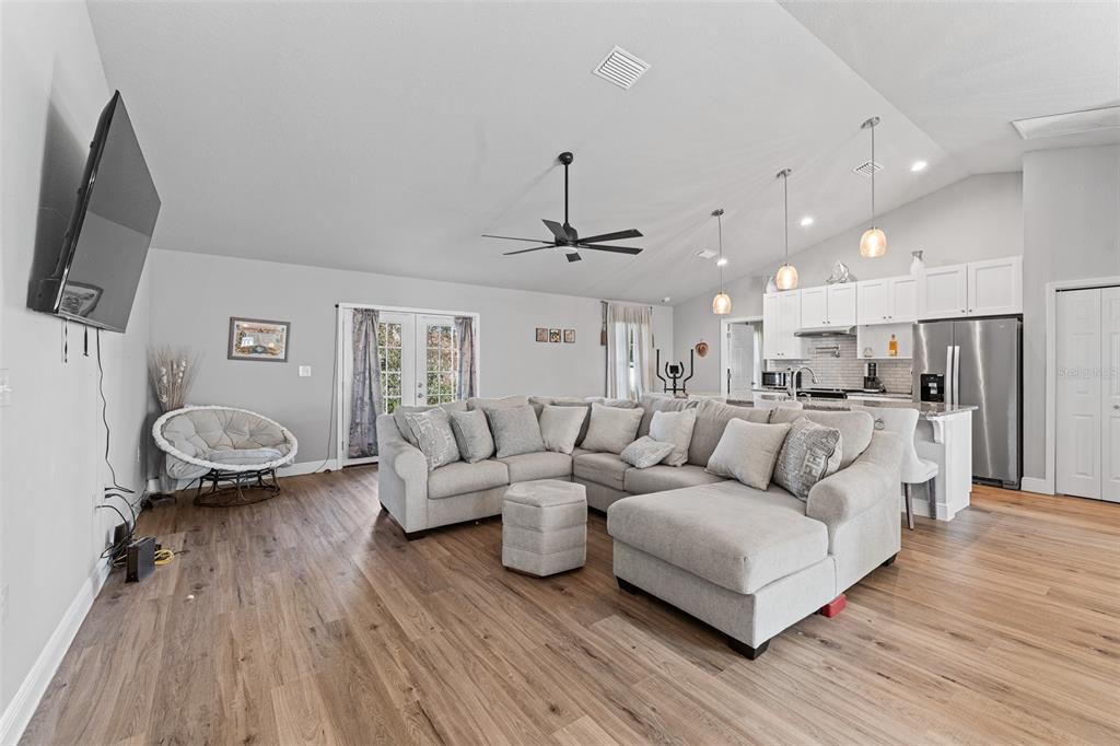 A spacious open-concept living room features a large sectional sofa, wood-look flooring, and kitchen — 1780 SW 168TH LOOP, OCALA, FL