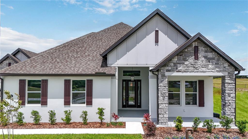 A one-story house with a white stucco facade, stone accents, and a dark shingled roof — 3836 SADDLE HILL TRAIL, FRUITLAND PARK, FL