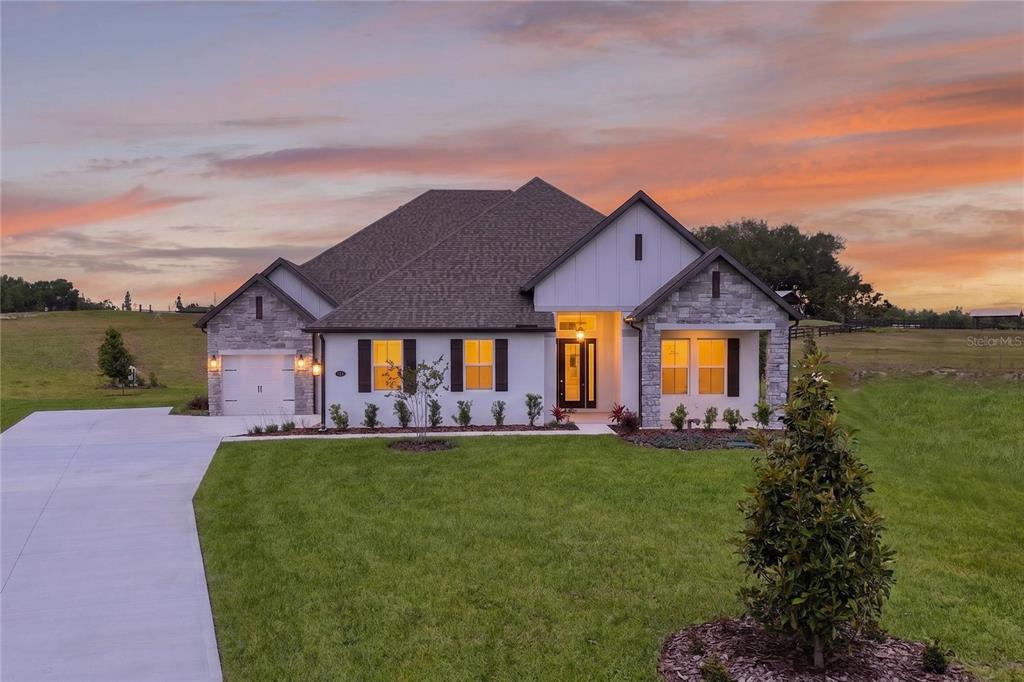 A single-story house with stone and white siding features a driveway and a grassy lawn — 3836 SADDLE HILL TRAIL, FRUITLAND PARK, FL