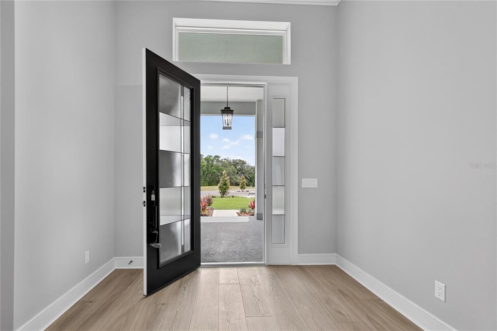An open front door reveals a view of a grassy yard from a light-floored entryway — 3836 SADDLE HILL TRAIL, FRUITLAND PARK, FL