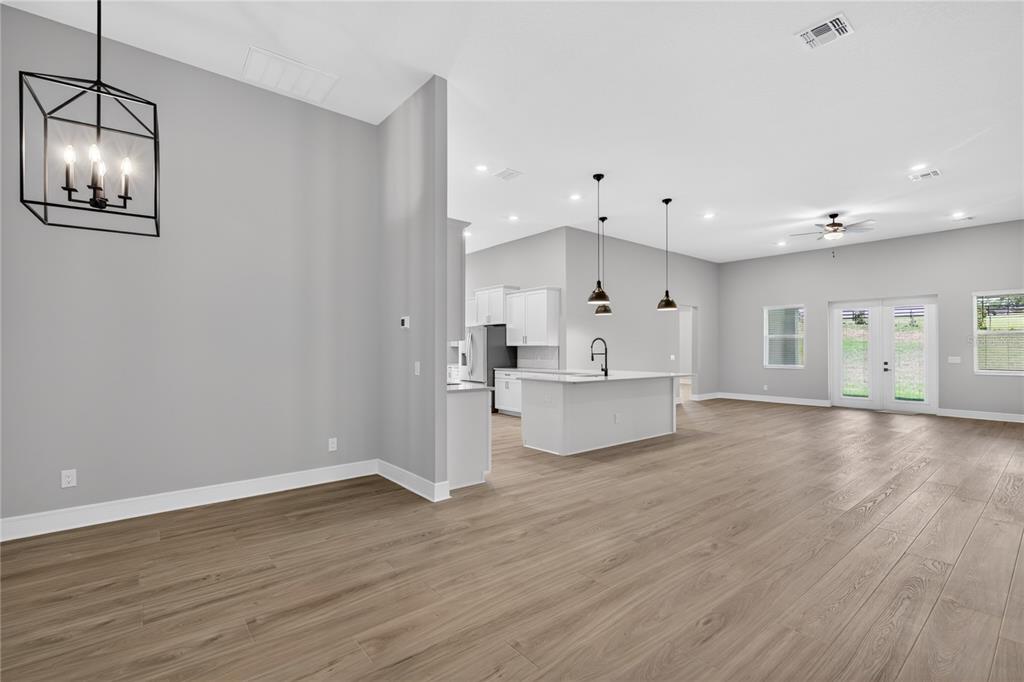 An open-concept living area features light gray walls, wood-look flooring, and a modern kitchen — 3836 SADDLE HILL TRAIL, FRUITLAND PARK, FL