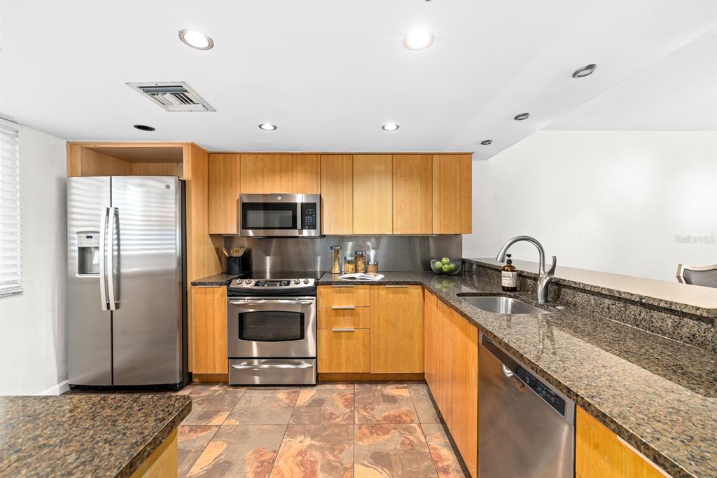 A kitchen features light wood cabinets, stainless steel appliances, granite countertops, and tiled flooring — 201 W LAUREL STREET UNIT 310, TAMPA, FL