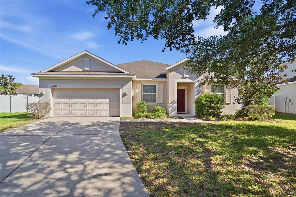 A single-story house with a two-car garage, beige stucco exterior, and a concrete driveway — 1520 RHODESWELL LANE, DOVER, FL