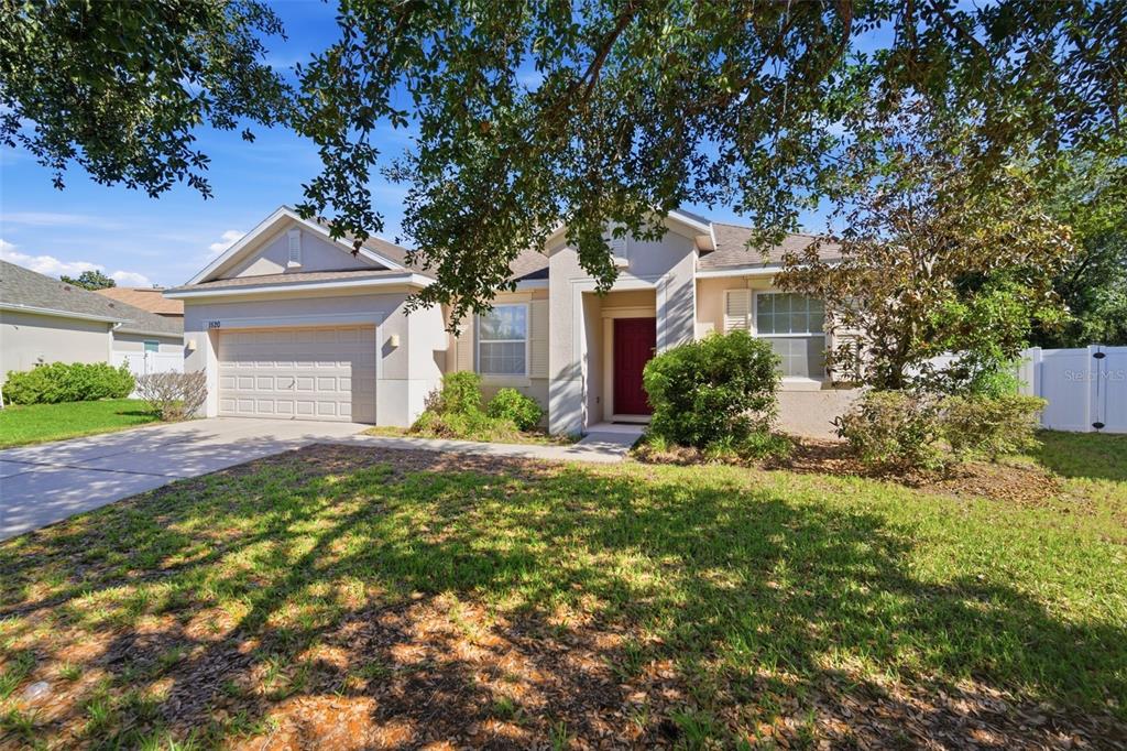 A single-story house with a beige exterior, a red front door, and a two-car garage — 1520 RHODESWELL LANE, DOVER, FL